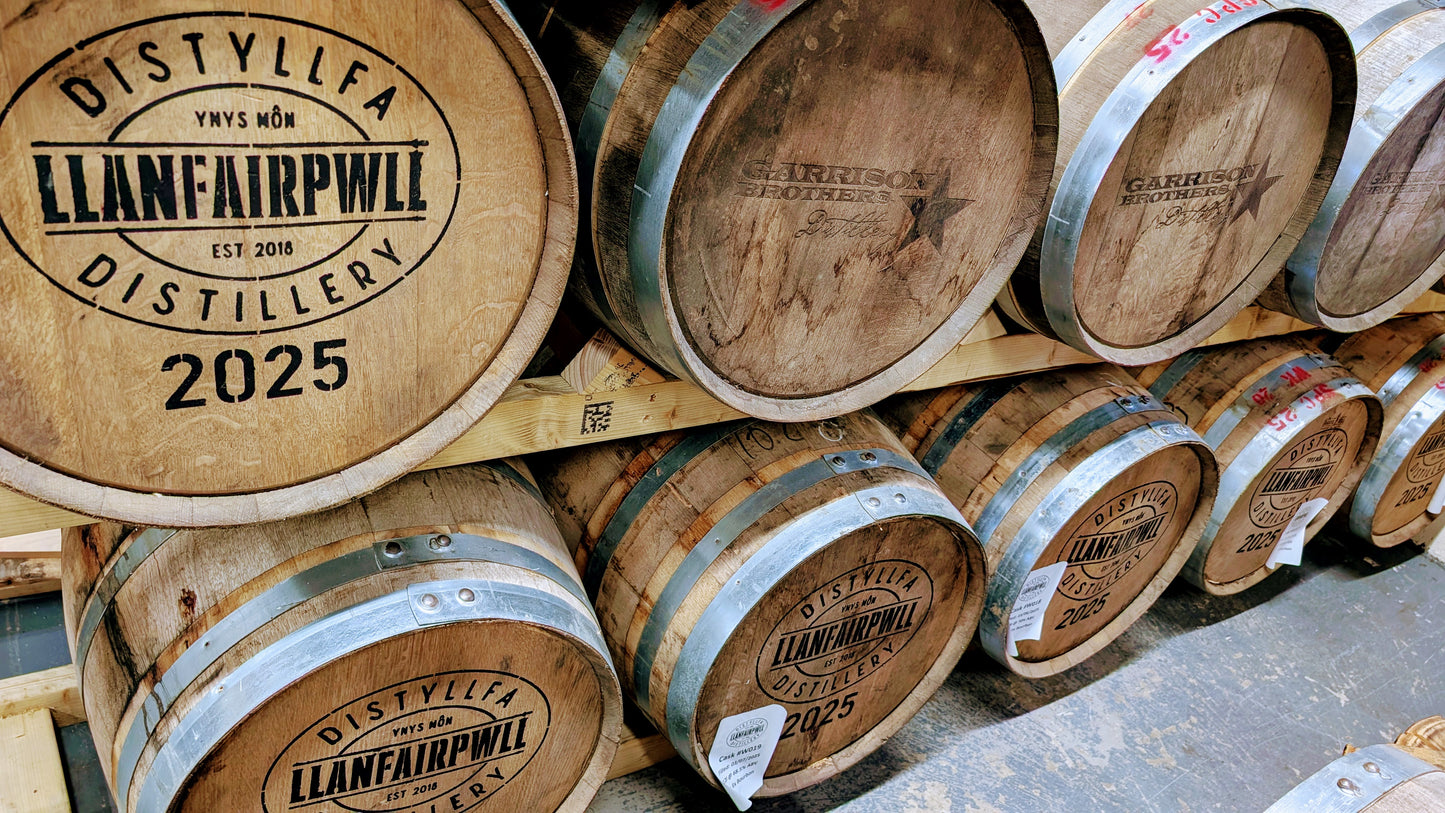Wooden barrels with 'Llanfairpwll Distillery' branding stacked together.